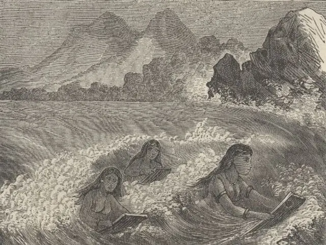The image shows three women in the ocean with mountains in the background. They are sitting in the...