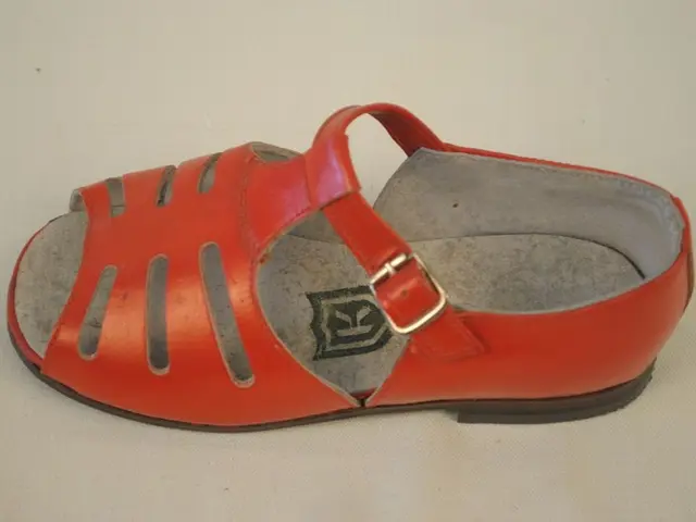 The image shows a pair of red sandals sitting atop a white surface. The sandals have a classic...