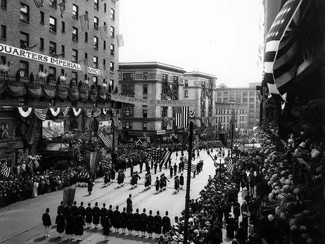The image shows a large crowd of people walking down a street in New York City during the Fourth of...