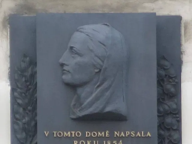 The image shows a plaque on the side of a building with a sculpture of a woman's face and text...