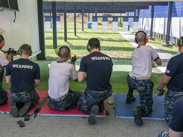 The image shows a group of men in military uniforms sitting on the ground, wearing headsets and...
