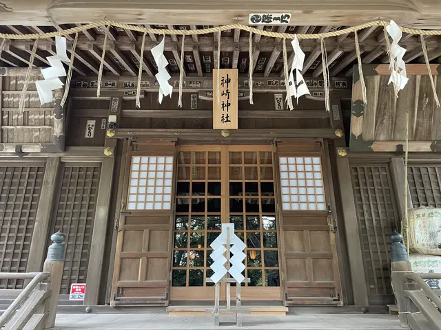 The image shows a large wooden building with a lot of windows and a door, a board with some text on...