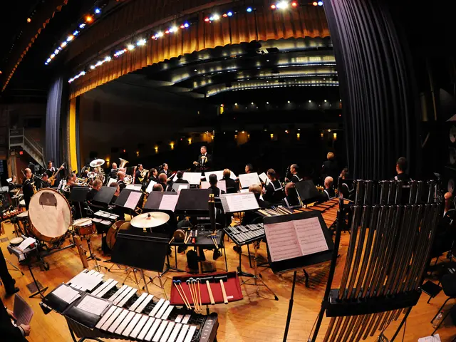The image shows a large orchestra in a large auditorium with a conductor and orchestra. There are...
