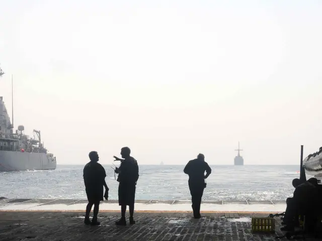 The image shows a group of people standing on top of a boat in the water, with a submarine on the...