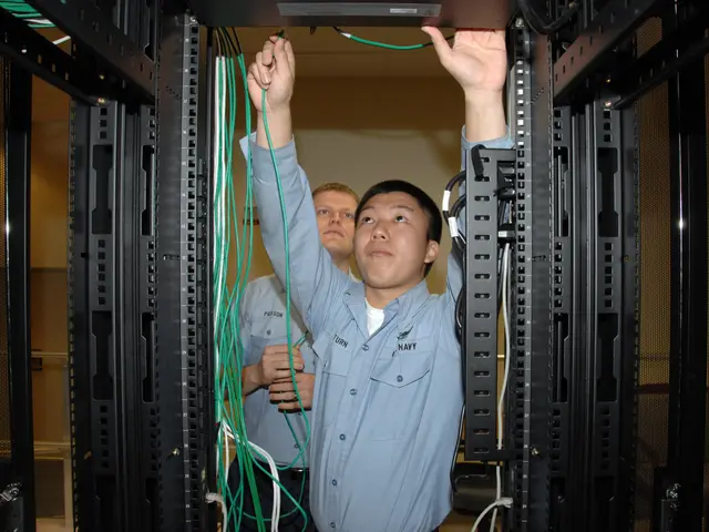 The image shows two men working on a server in a data center, surrounded by racks of cables and a...