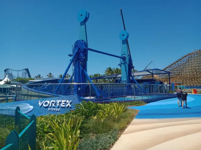 The image shows a group of people walking down a path next to a roller coaster, surrounded by...