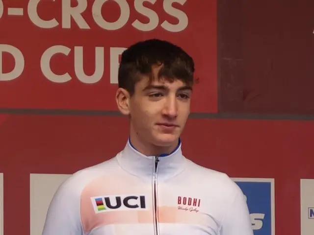 The image shows a man standing on top of a podium, holding a bouquet of flowers in his hands, with...