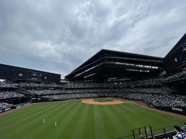 The image shows a baseball game being played in a large stadium, with a group of people on the...