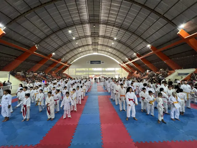 The image shows a large group of people standing on top of a blue and red mat in a gymnasium. There...