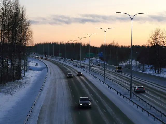 The image shows a highway with cars driving down it in the snow, surrounded by railings, light...