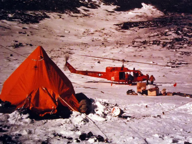The image shows a helicopter parked next to a red tent in the snow, with a few people standing...
