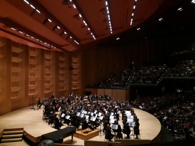The image shows a large auditorium filled with lots of people watching a concert. There are many...
