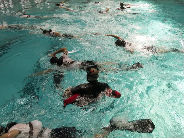The image shows a group of people swimming in a pool with their backs to the camera, wearing...