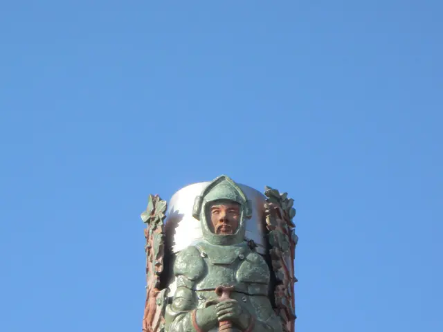 The image shows a statue of a man in armor on top of a building, with a clear blue sky in the...