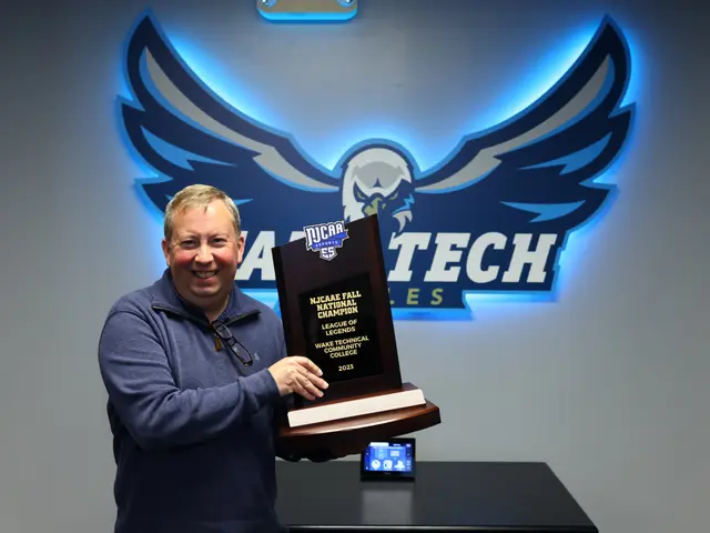 The image shows a man standing and smiling while holding a plaque in front of a wall with a logo...