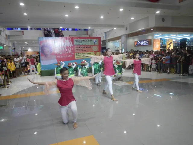 The image shows a group of young girls in pink shirts and white pants dancing in a mall, surrounded...