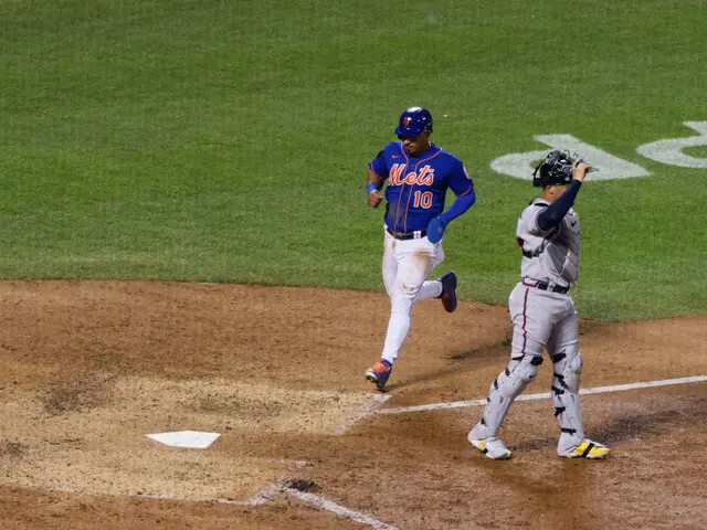 The image shows a baseball player running towards home plate during a game. The player is wearing a...