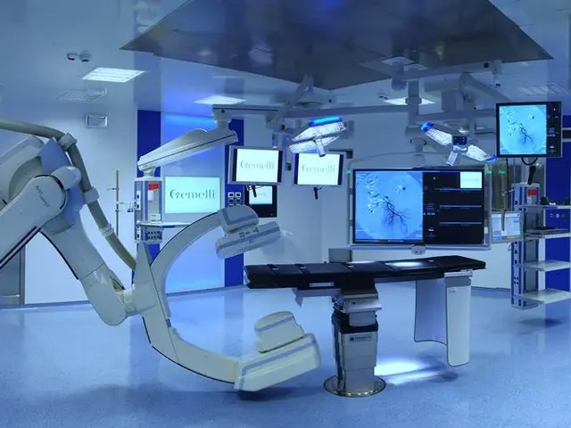 The image shows a hospital room with a robotic arm in the middle of it, surrounded by monitors and...