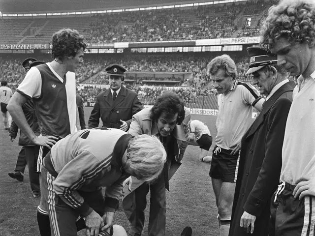 The image shows a group of men standing around a soccer player laying on the ground, surrounded by...