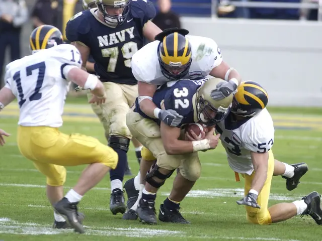 The image shows a football player being tackled by a group of defenders on a grassy field. The...
