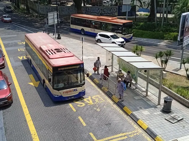The image shows a city street with cars and buses driving down it. There is a bus stop on the side...
