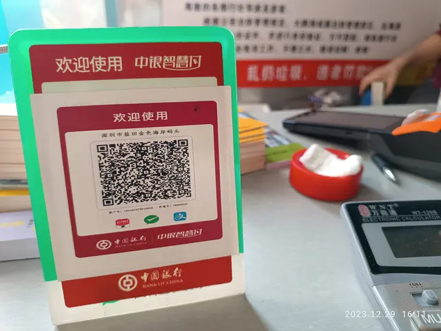 The image shows a person standing in front of a table with a QR code on it. On the table there are...