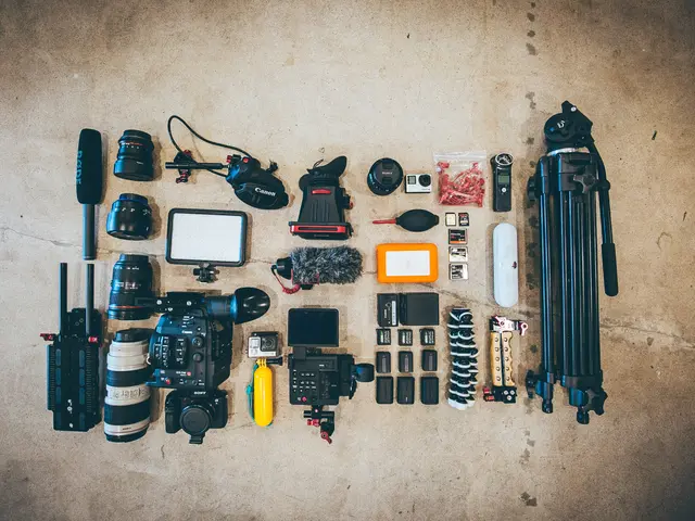 The image shows a variety of camera equipment laid out on the floor, including a camera, camera...