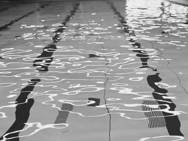 The image shows a black and white photo of a swimming pool with water ripples on the surface. The...