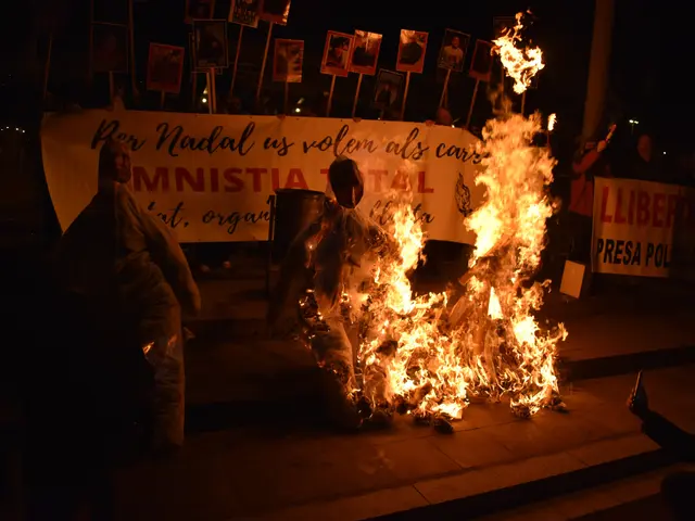 The image shows a group of people standing around a bonfire in the middle of a street at night. The...