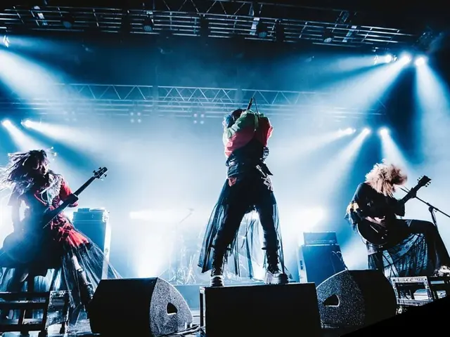 The image shows a group of people on stage playing guitars and singing, surrounded by mics with...