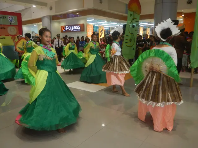 The image shows a group of people in green and pink dresses dancing in a mall, surrounded by a...