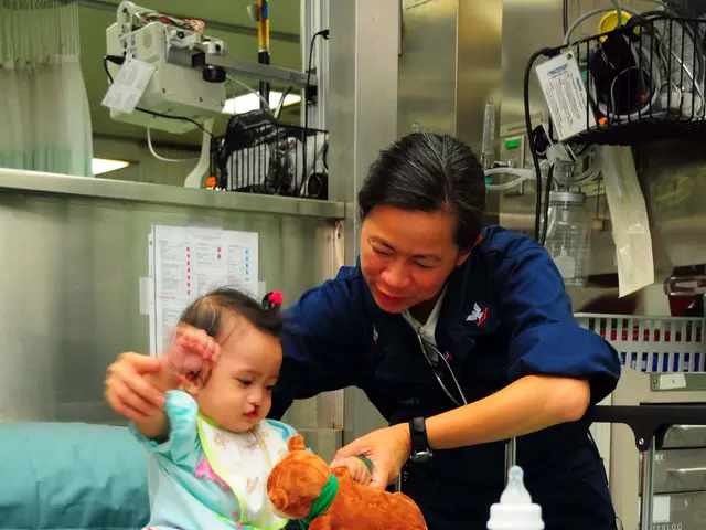 The image shows a woman in a hospital room with a baby lying on a bed surrounded by toys, a bottle,...