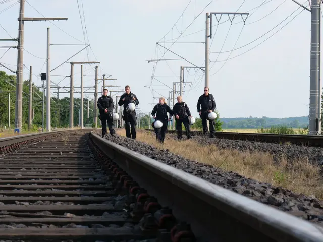 The image shows a group of police officers walking down train tracks, each holding a helmet in...
