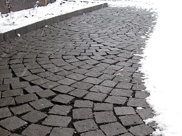 The image shows a cobblestone street with snow on the ground and a fence in the background. The...