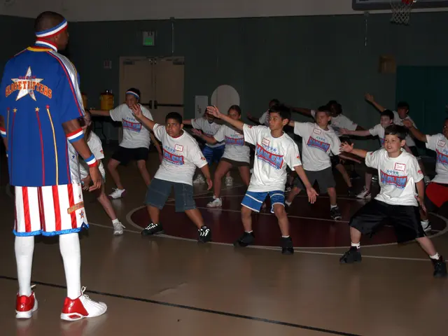 The image shows a group of young boys playing basketball in a gymnasium. We can see a man standing...