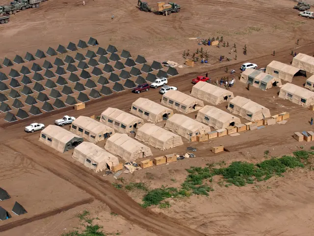 The image shows an aerial view of a large group of tents in the middle of a desert, surrounded by...