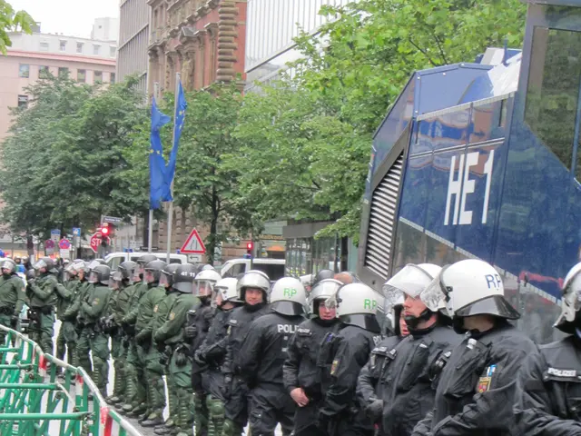 The image shows a group of police officers standing in front of a barricade, wearing helmets and...