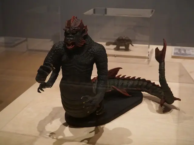 The image shows a statue of Godzilla on display in a glass case, surrounded by other toys on the...