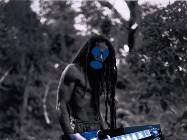The image shows a man with dreadlocks standing in the woods, playing a guitar. He is surrounded by...