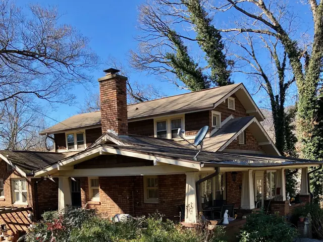 The image shows a house with a roof that has been damaged by a storm, surrounded by plants, grass,...