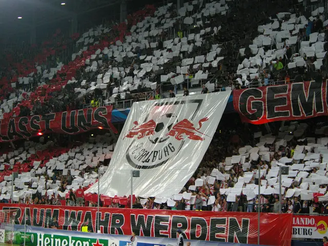 The image shows a soccer stadium filled with lots of people, some sitting on chairs and some...