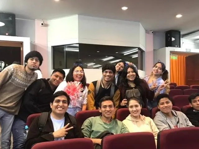 The image shows a group of people posing for a photo in a movie theater. There are a few people...