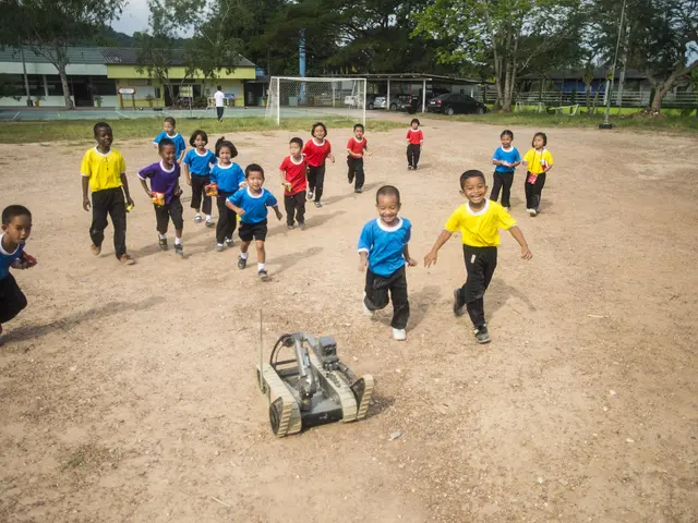 The image shows a group of children playing soccer on a dirt field surrounded by trees, buildings,...