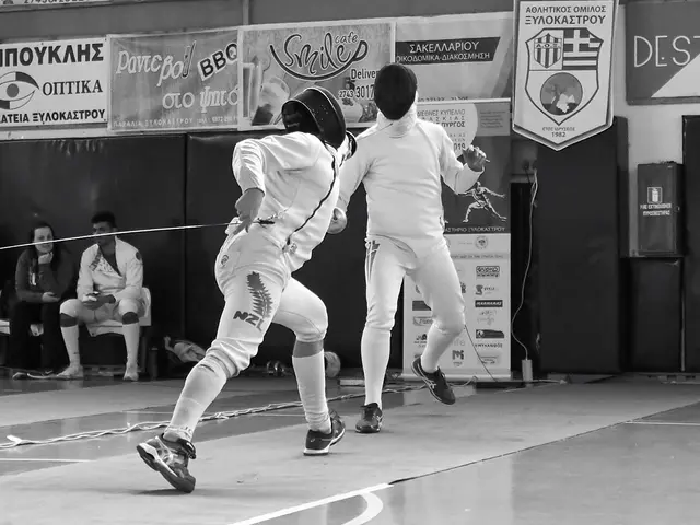 The image shows two men fencing in a gymnasium with a crowd of people watching. They are both...