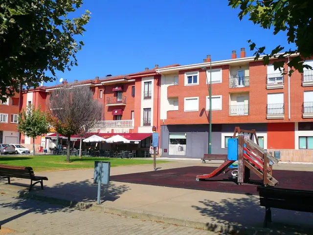 The image shows a park with a playground in the middle of it, surrounded by buildings with windows,...