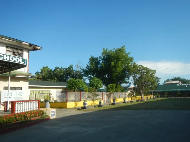 The image shows a school building with a sign on the side of it, surrounded by a road, grass,...