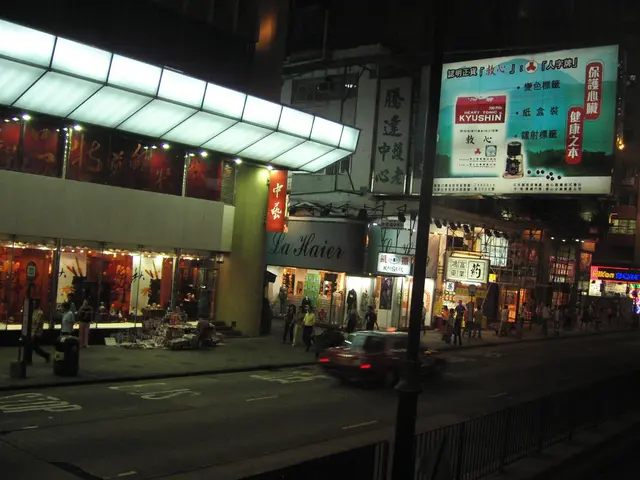 The image shows a bustling city street at night with a car driving down the road, surrounded by...