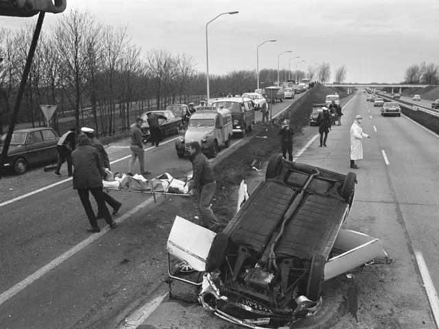 The image shows a black and white scene of a car that has been flipped over on the side of the...