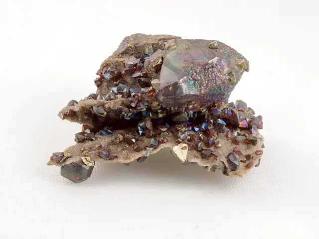 The image shows a piece of pyrite on a white surface, with its iridescent colors shimmering in the...