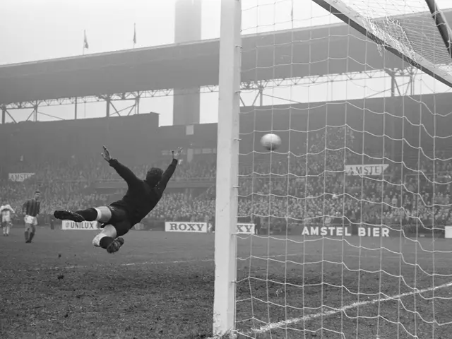 The image shows a black and white photo of a soccer player making a save in front of a goal, with a...